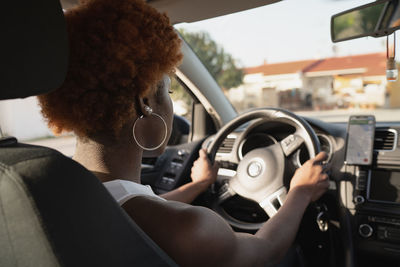 Back view of black female with afro hairstyle sitting on driver seat in sunny day