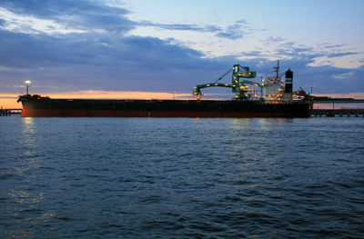 Scenic view of container ship in harbour against sky at dusk