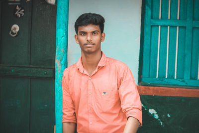 Portrait of young man standing against door