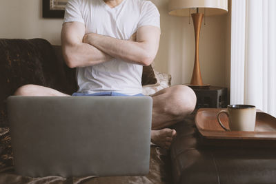 Midsection of man using mobile phone while sitting on sofa at home