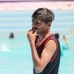 Young man looking away while standing by swimming pool