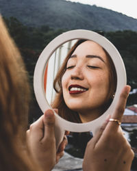 Close-up portrait of a smiling young woman holding reflection