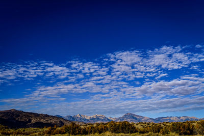 Patchy cloud layers in blue sky above mountain peaks in autumn valley landscape