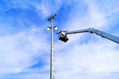 Low angle view of man standing on cherry picker by floodlight against sky