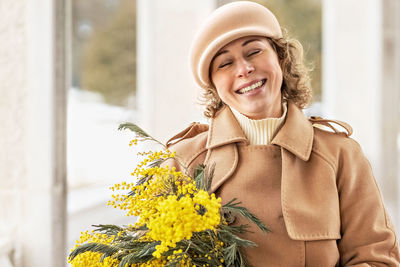 A young woman in a beige coat and hat with a bouquet of mimosa. international women's day