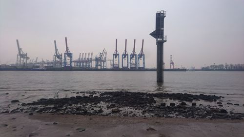 Cranes at harbor against sky