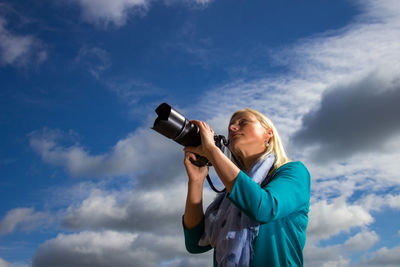 Low angle view of woman photographing with camera against sky