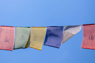 Low angle view of prayer flags hanging against clear blue sky