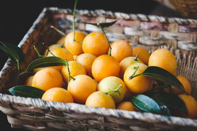 High angle view of plums in basket on wooden table against black background