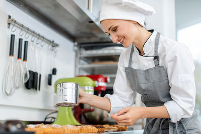 Woman holding food while standing at kitchen