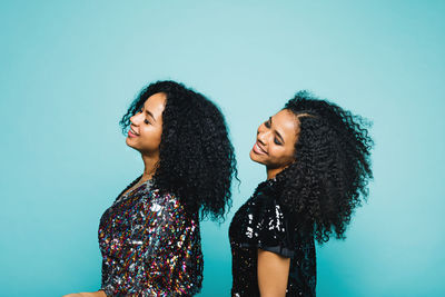 Side view of sisters standing against blue background