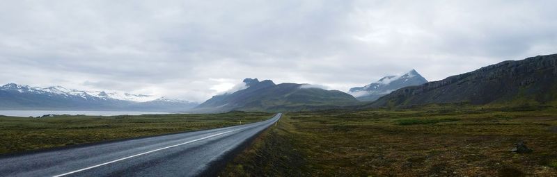 Dirt road passing through landscape against cloudy sky