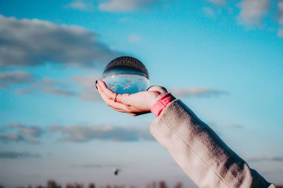 Cropped hand holding crystal ball against sky