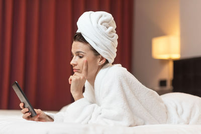 Side view of woman wearing towel while using mobile phone on bed at home