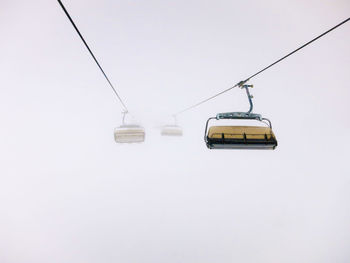 Low angle view ski lifts in foggy weather against clear sky