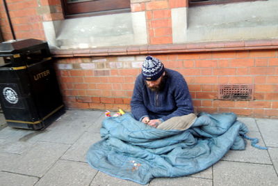 Beggar man with blanket sitting by building at footpath