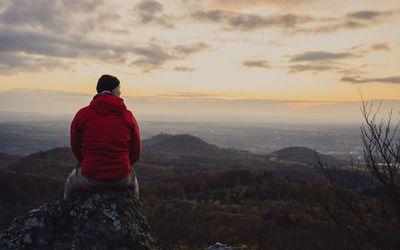 Rear view of man siting on mountain against sky