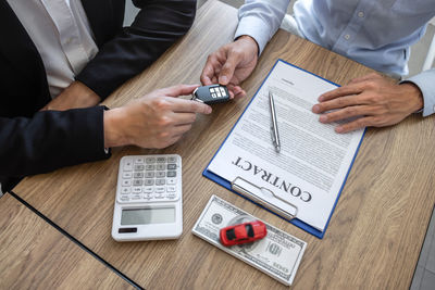 Agent giving car key to customer by papers and currency on table