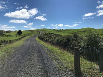 Dirt road amidst field against sky