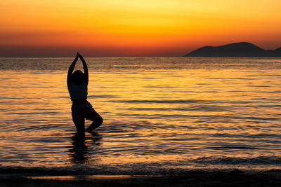 Silhouette person in sea against sky during sunset