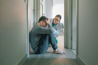 Side view of young woman looking through window at home