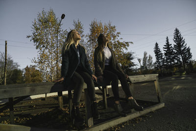 Two friends walking outdoors in autumn, the girls are sitting on a wooden bench, enjoying the sun