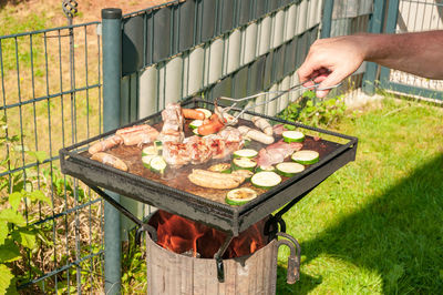 Cropped hand of man cooking meat on barbecue grill in yard