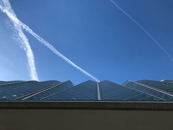 Low angle view of building with vapor trail against blue sky