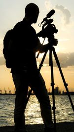 Silhouette man standing by sea against sky during sunset