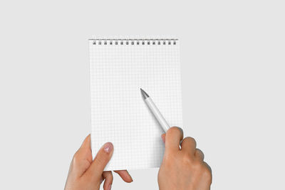 Cropped hand of woman writing in book against white background