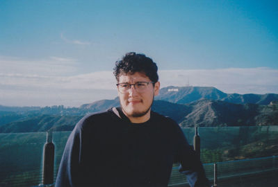 Young man standing by railing against mountains and sky