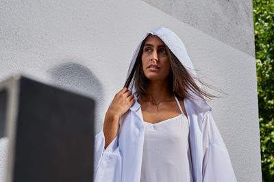 Portrait of young woman standing against white wall