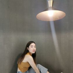 Portrait of young woman sitting against wall indoors