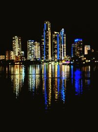 Illuminated buildings by river against sky at night