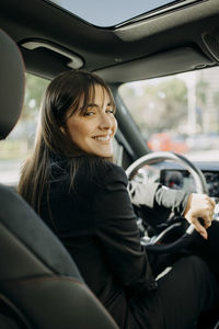 Smiling businesswoman sitting inside electric car