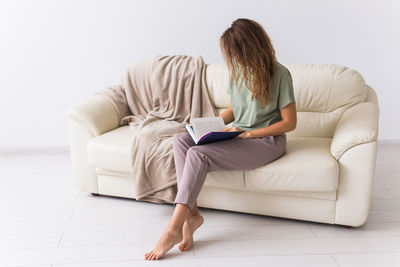 Full length of woman reading book sitting on sofa