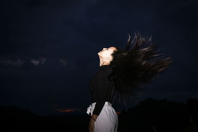 Side view of woman tossing hair standing outdoors at night