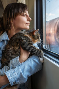 Smiling happy woman and cute fluffy kitten traveling together, tripping riding on electric train