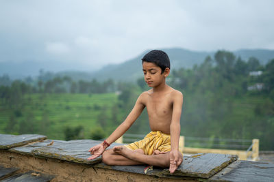 A young indian cute kid doing yoga in the mountains,wearing a dhoti.