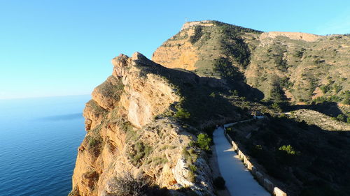 Scenic view of mountain by sea against clear blue sky