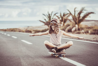 Cheerful boy sitting on skateboard against sky