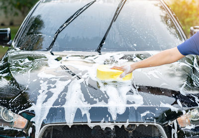 Detail of a sponge wipe a black car during a car wash at home.