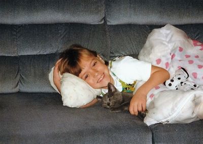 Portrait of girl relaxing with cat on sofa at home