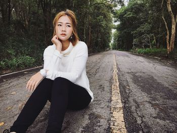 Portrait of young woman sitting on road against trees