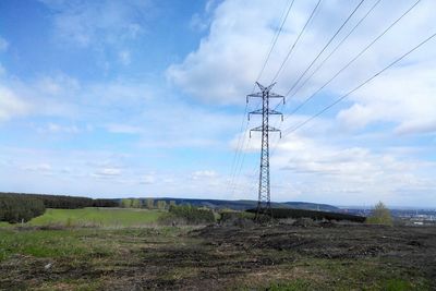 Electricity pylon on field against cloudy sky