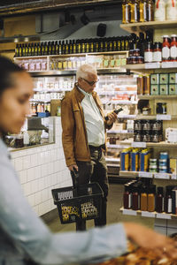 Senior man standing with shopping basket and bottle at convenience store