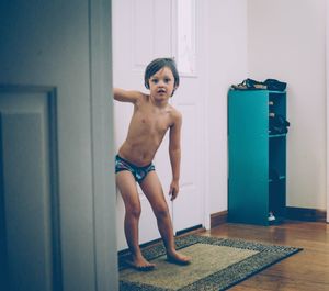 Portrait of shirtless boy standing against wall at home