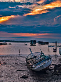 Boat moored on beach against sky during sunset