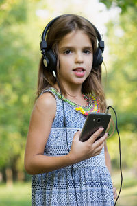 Smiling girl listening music while standing at park