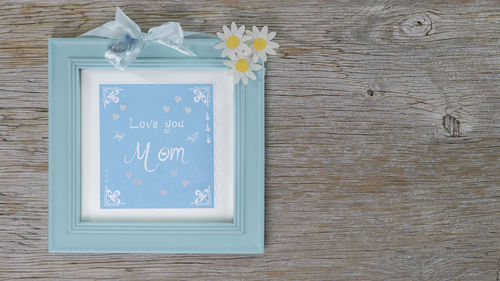 Frame with hand lettering text in english love you mom. wood background. flowers of the magerite.